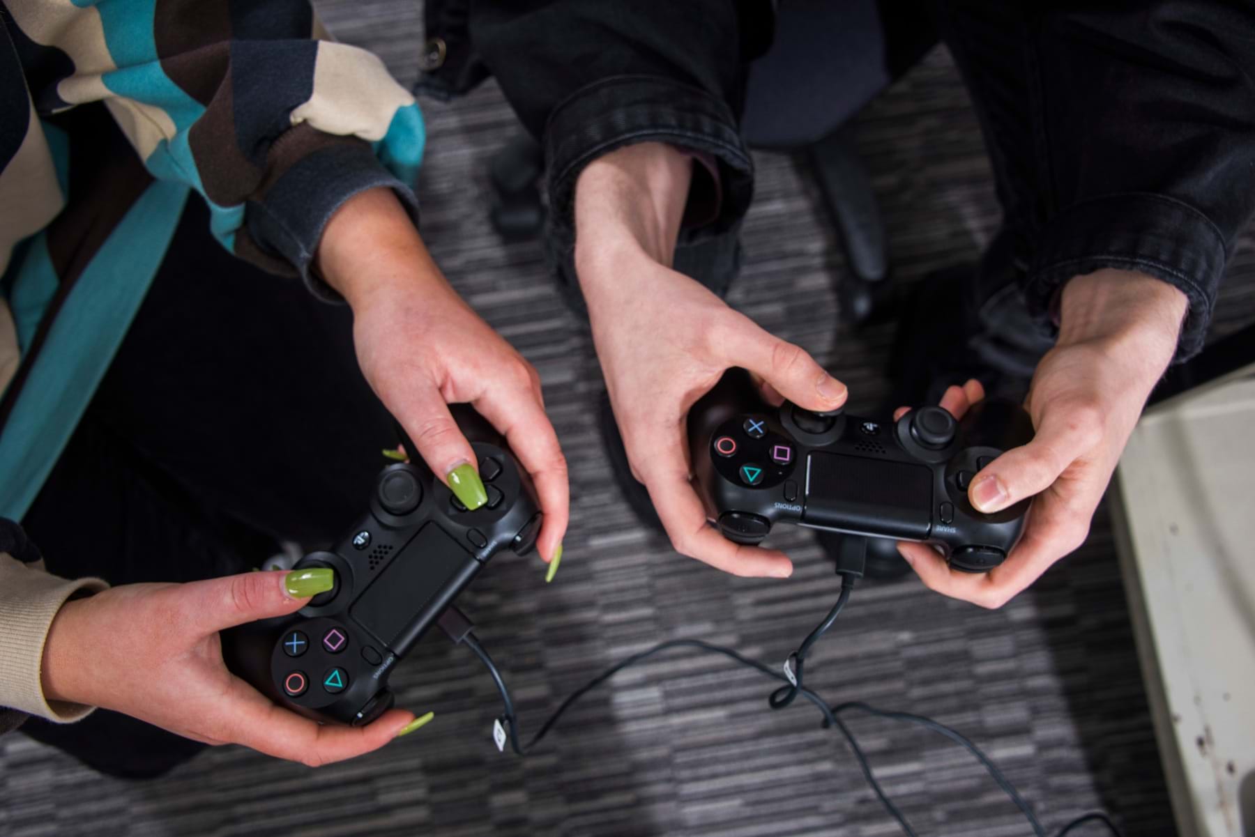 The image shows two hands showing two game pads. One of the hands has painted nails.