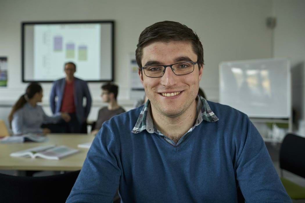 Male in a classroom smiling - 3 people in background