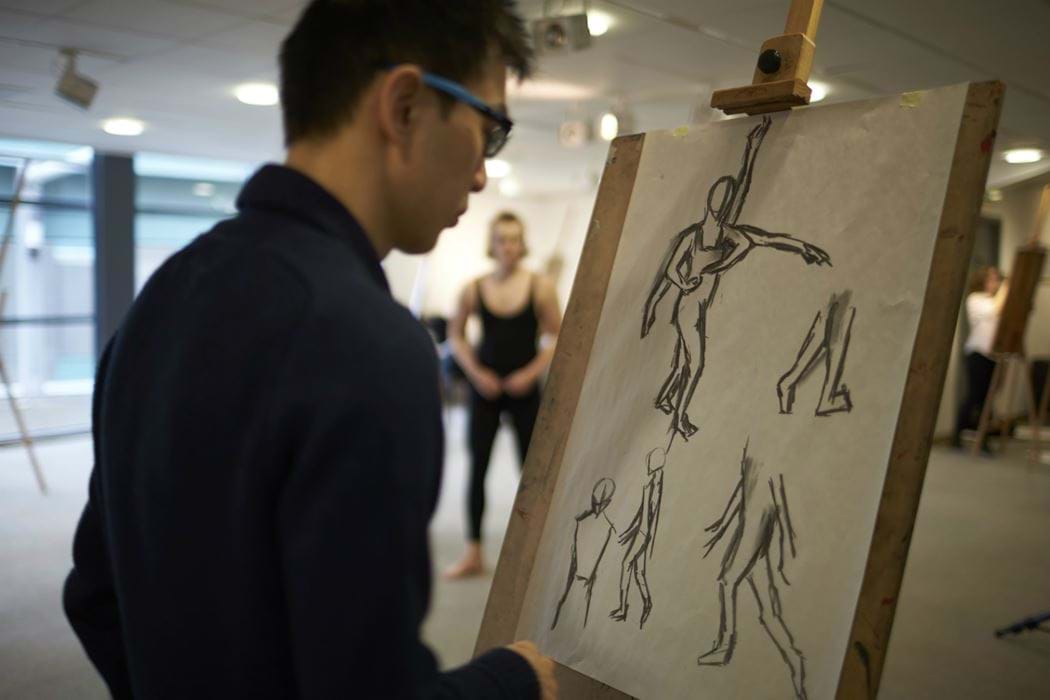 male drawing using an easel - live model in background