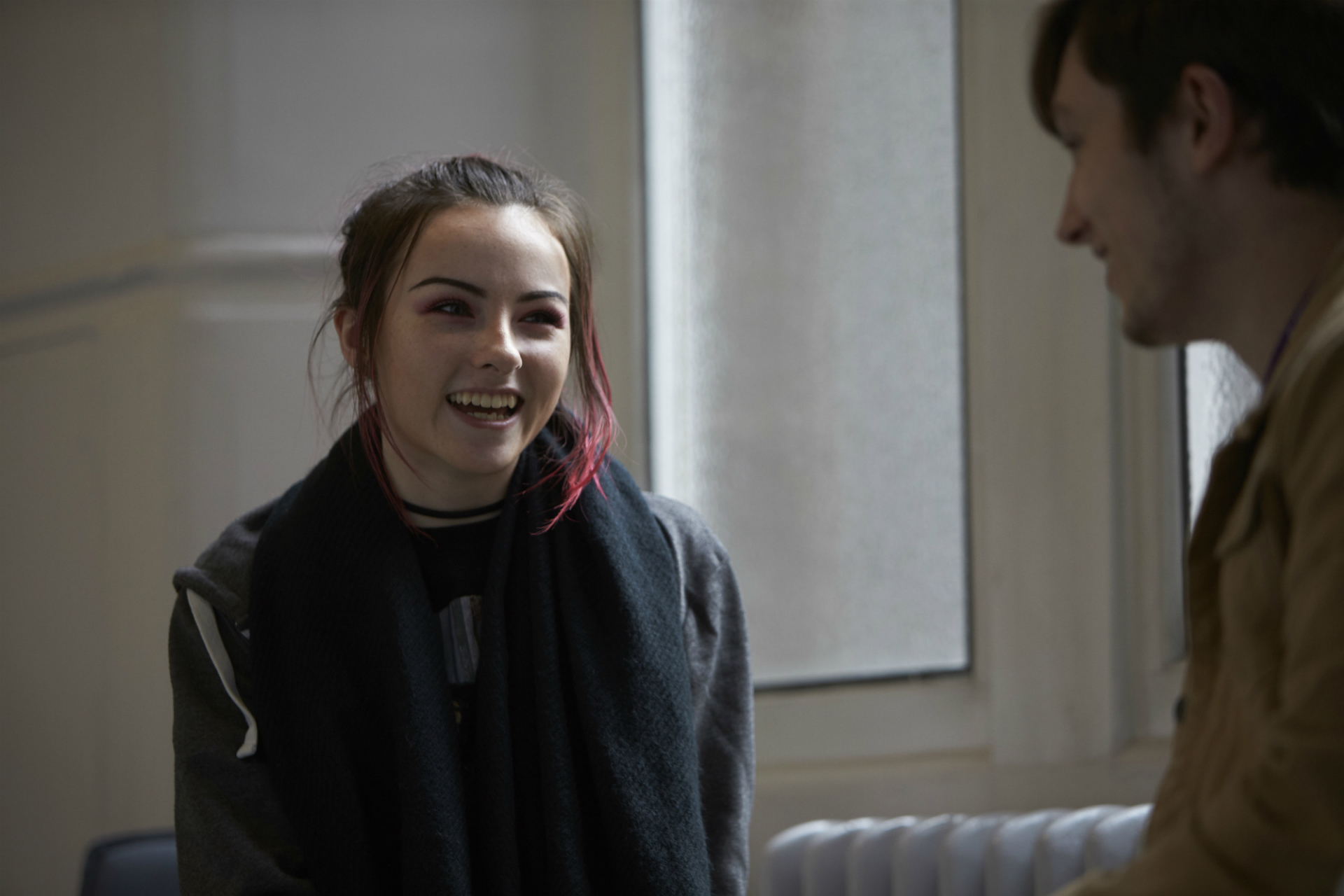 A student laughing, wearing a black jacket and with brown and red hair