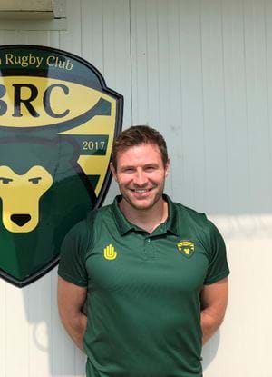 Fraser Murray next to the green and yellow Biella Rugby Club logo wearing a team shirt