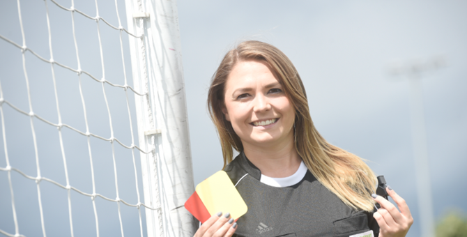 Vikki in FIFA Assistant Referee uniform holding a whistle and cards