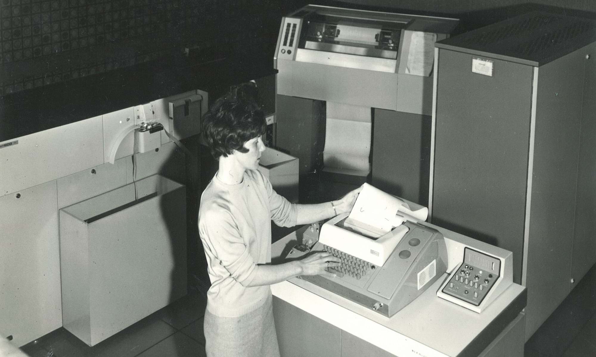 Female staff member at Dundee Institute of Art and Technology (Abertay University) looking at data being printed from a computer in the 1960s