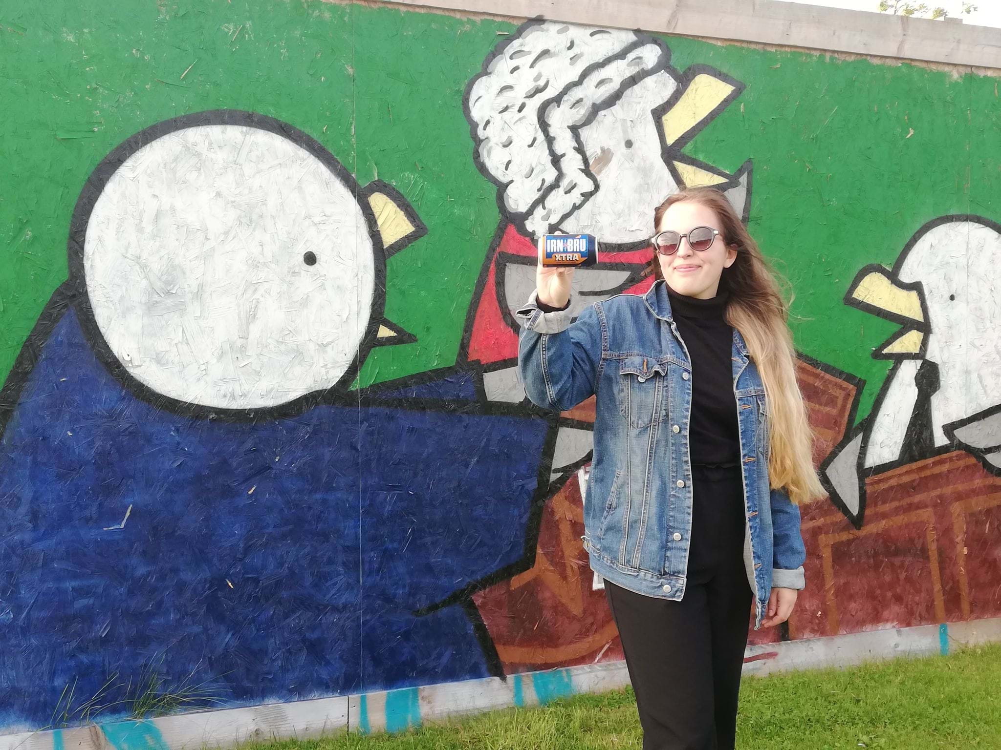 A photo of Barbara Szpilka holding a can of Irn Bru in front of seagull grafitti