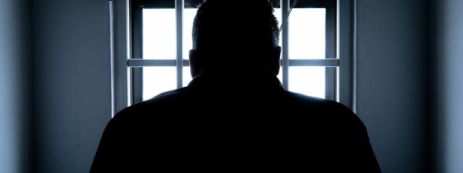 Image shows the silhouette of a man in a prison cell