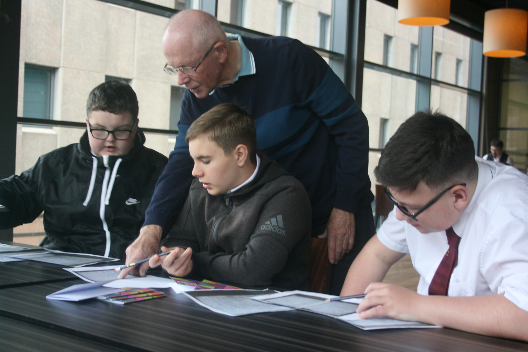 The image shows school pupils working at a desk with help from a lecturer.
