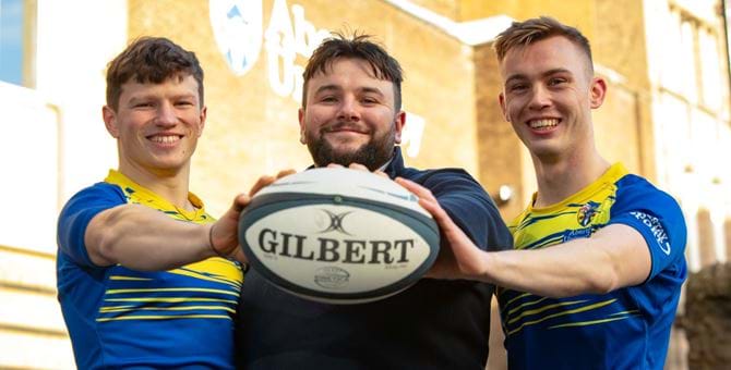 3 rugby club members holding ball towards viewer
