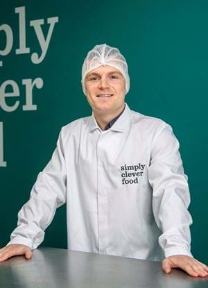 Jamie Mcdonald standing in front of a wall with "simply clever food" written on it
