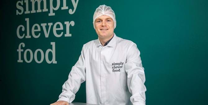 Jamie Mcdonald standing in front of a wall with "simply clever food" written on it