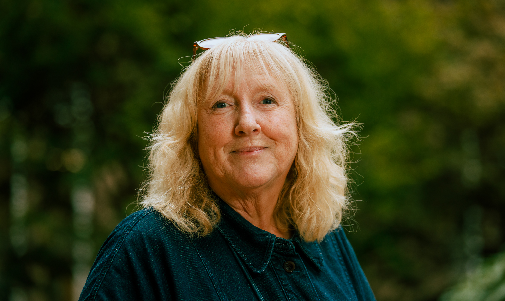 Professor Mhairi Thurston pictured on the Abertay campus. Wearing a red top, she smiles warmly to the camera. The walls behind her are white and bright.