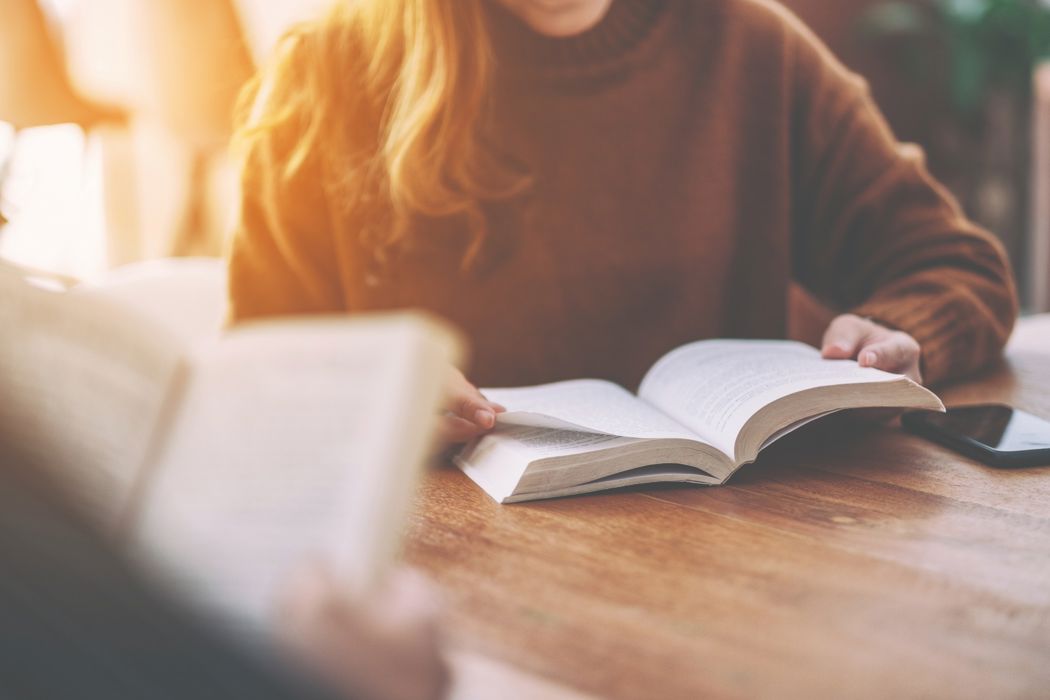 A female reads a book while sitting at a wooden table