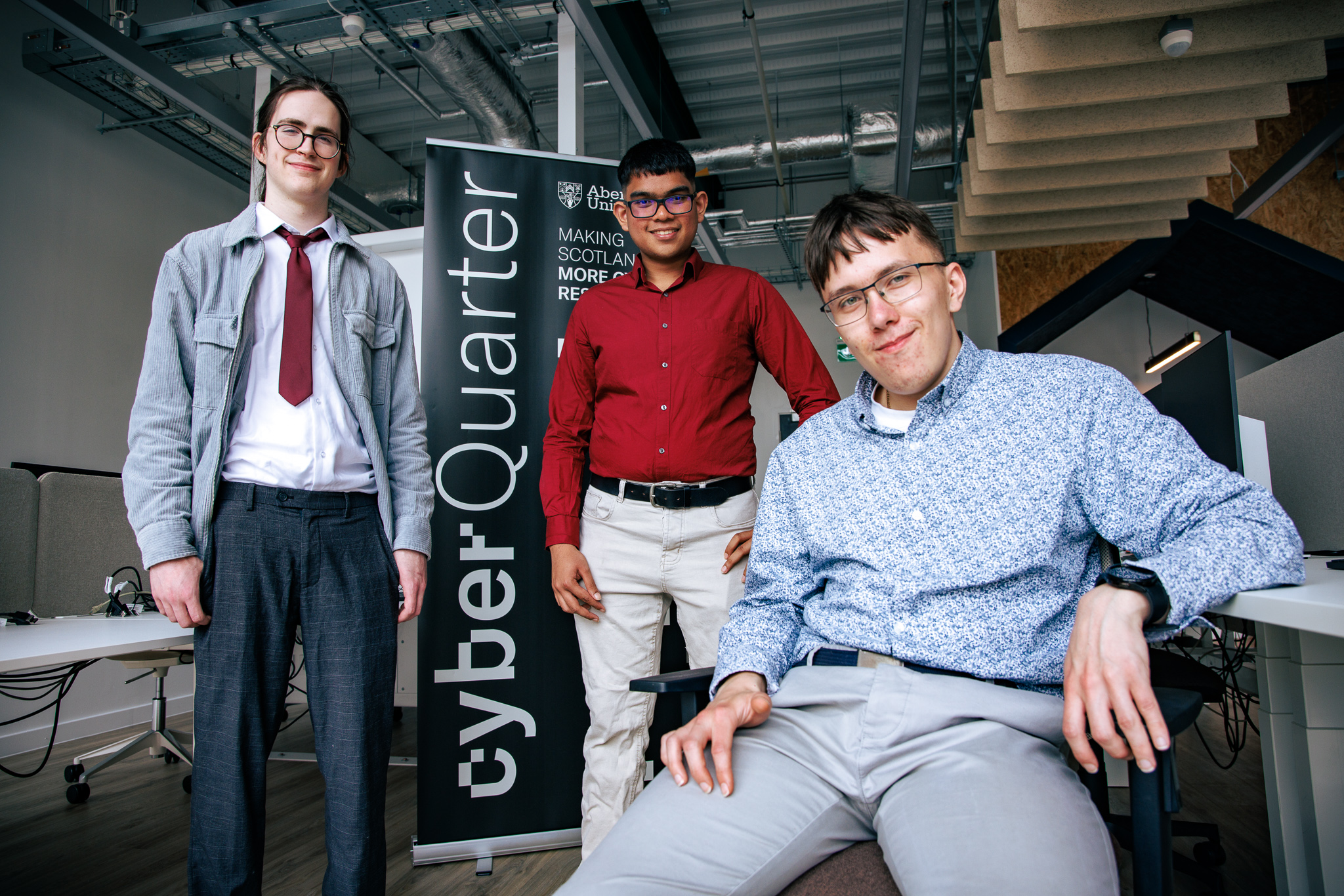 Student on chair in foreground with two students standing behind him in Abertay cyberQuarter